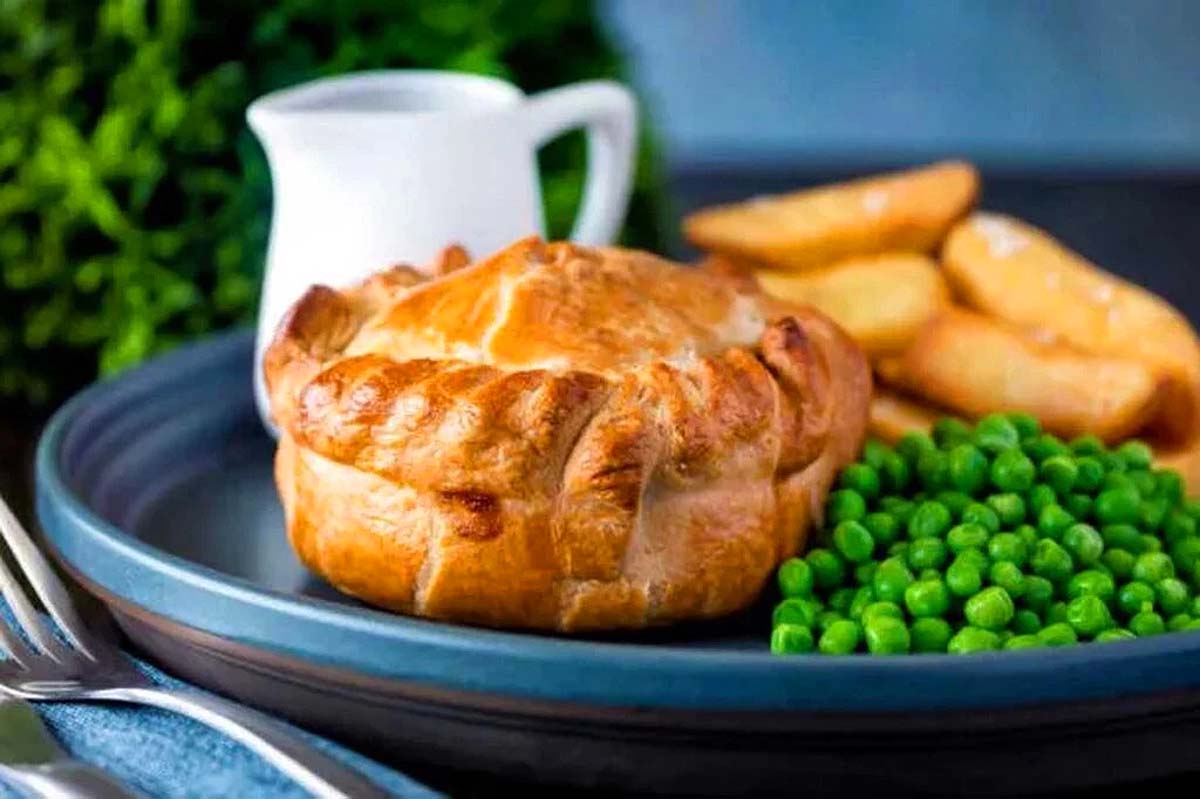 A plate with a traditional pub food dish of pie and peas on it.