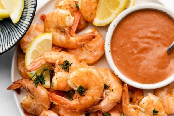 Shrimp on a plate with sauce and lemon wedges.