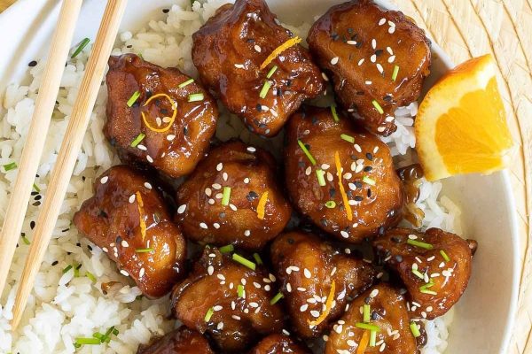 Asian chicken with orange slices and chopsticks on a white plate.