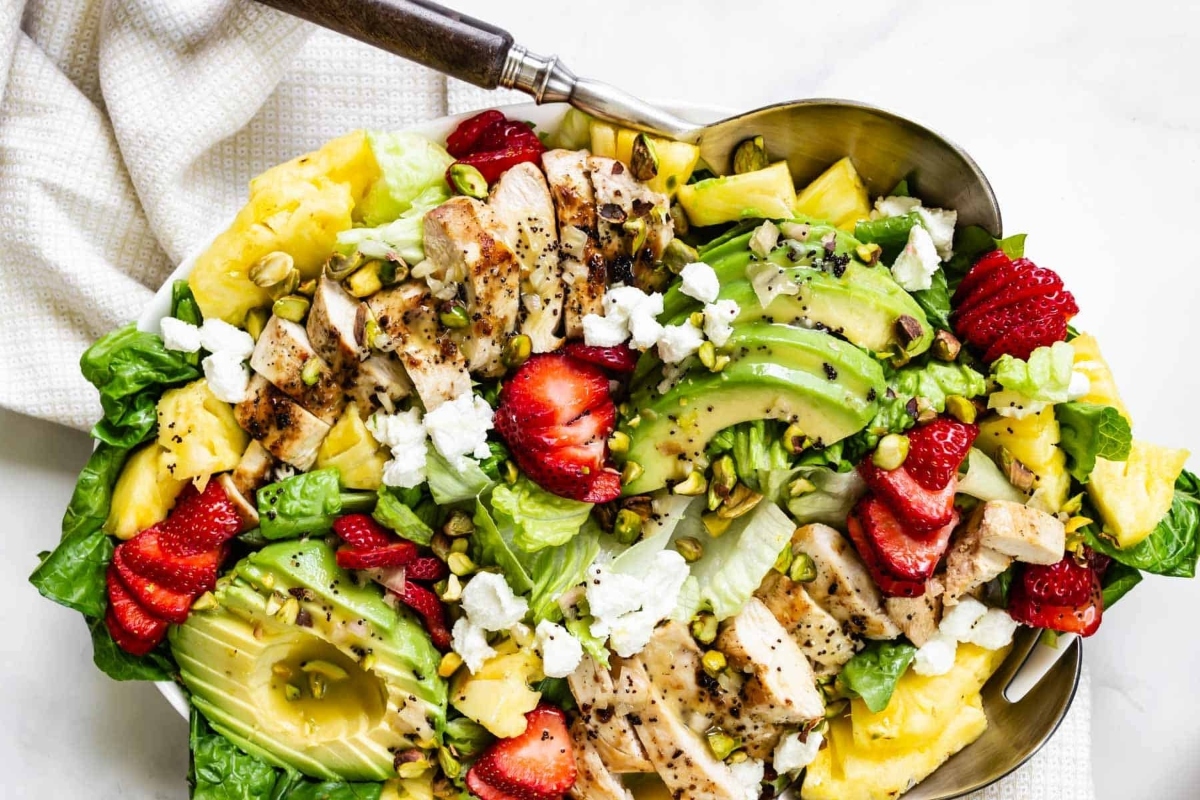 A salad with chicken, avocado, strawberries and pistachios.