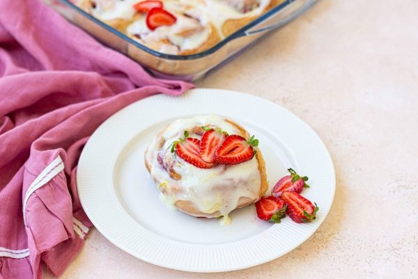 Strawberry cinnamon rolls on a plate with strawberries and cinnamon rolls.