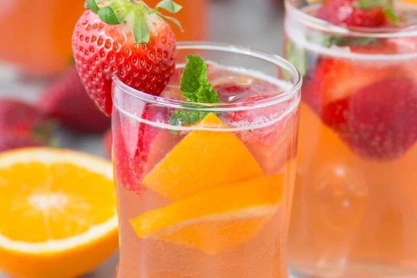 A glass of sangria with strawberries and oranges.