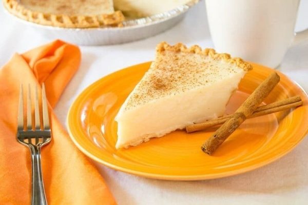 A slice of pie on an orange plate with cinnamon sticks.