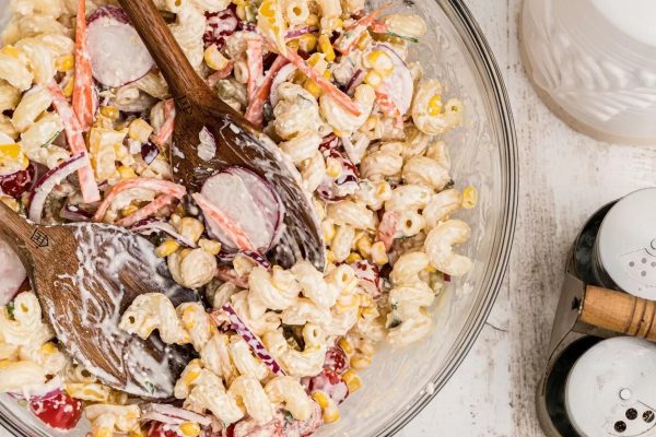 A bowl of pasta salad with corn and radishes.