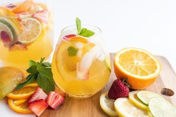 A glass of sangria with fruit and mint.