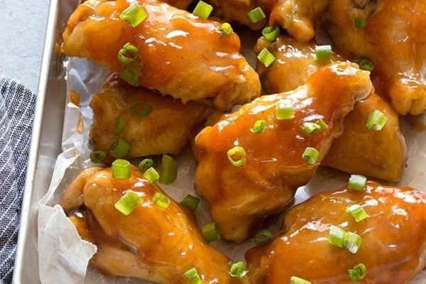 Game day chicken wings in a baking pan with sauce and green onions.