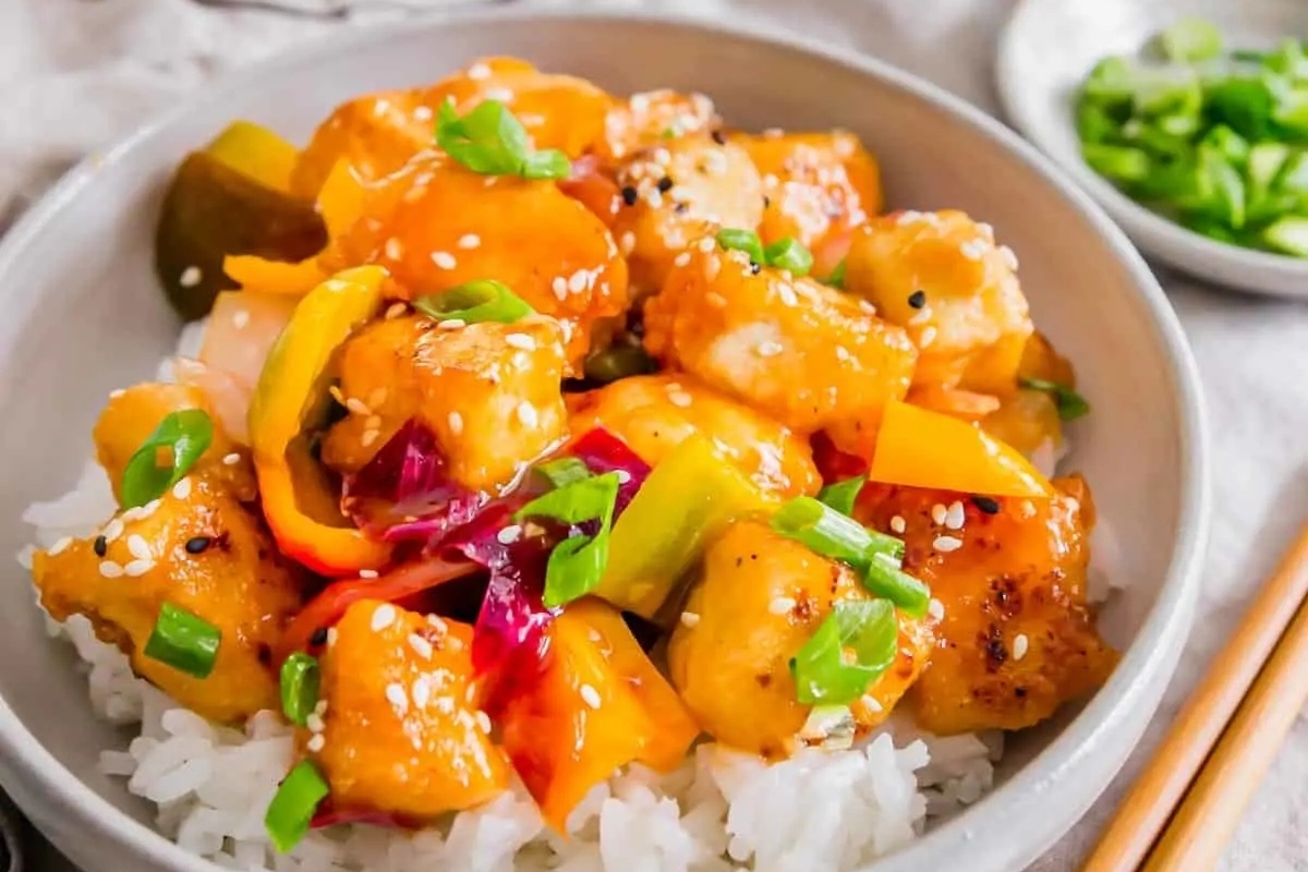 A bowl of asian chicken stir fry with rice and peppers.