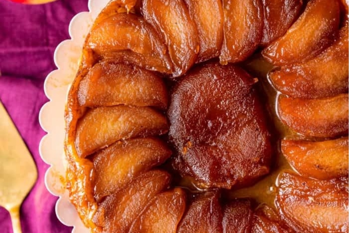 A slice of apple upside down cake on a plate with a gold fork.
