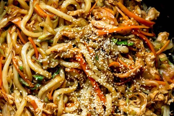 A skillet filled with noodles, carrots and sesame seeds.
