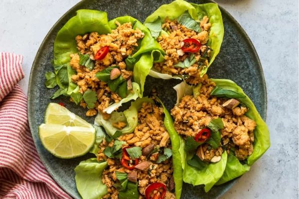 Thai chicken lettuce wraps on a plate with lime wedges.