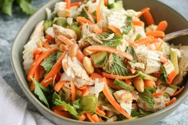 A bowl of asian chicken salad with carrots and peanuts.