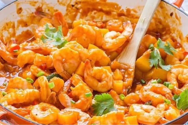 A pan full of shrimp in a sauce with a wooden spoon.
