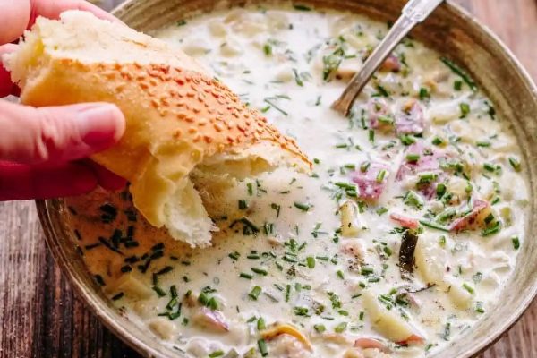 A hand is holding a bowl of cream soup.