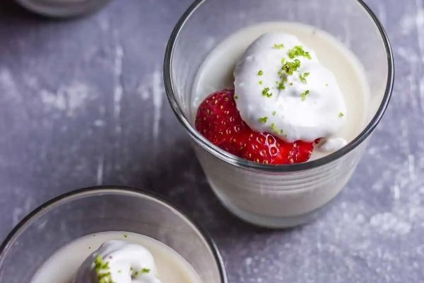 Two coconut desserts topped with whipped cream and strawberries.