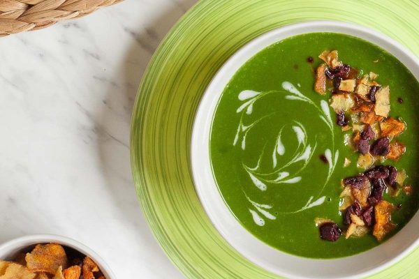 A creamy bowl of green soup with crackers on a plate.