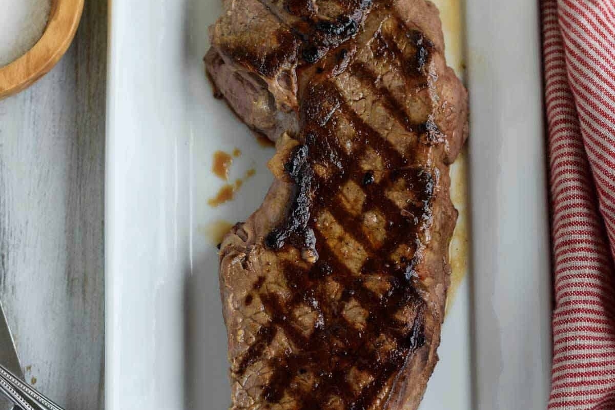 A dinner party main featuring a steak on a white plate, perfectly seasoned with salt and pepper.