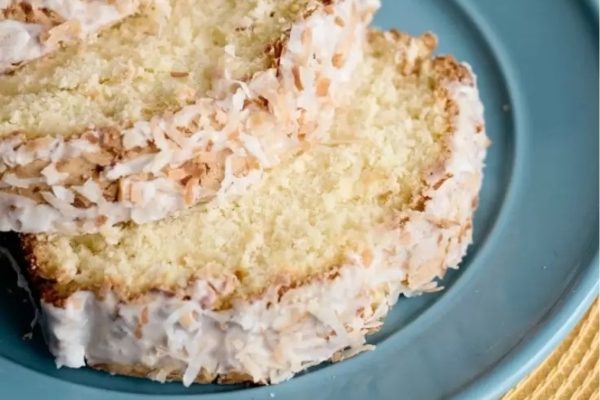 A slice of coconut pound cake on a blue plate, topped with shredded coconut.