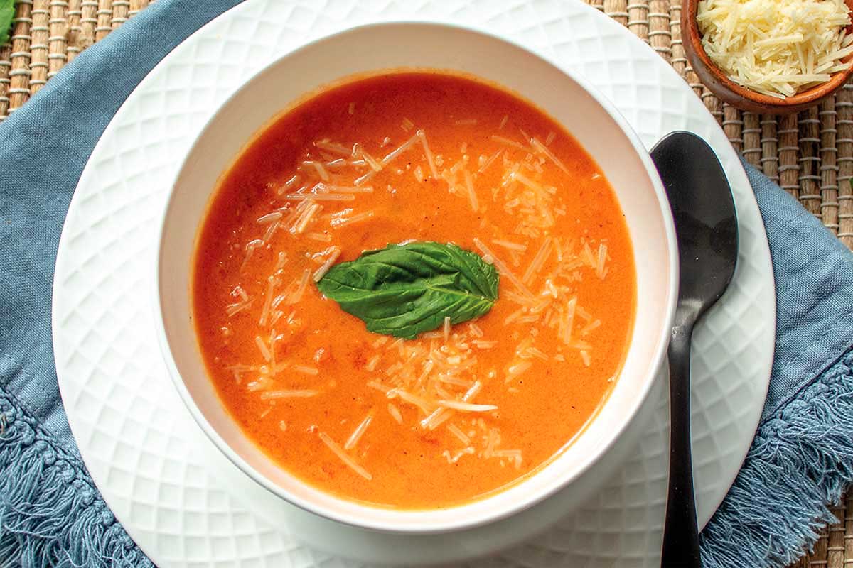 A bowl of tomato soup with parmesan cheese and basil.