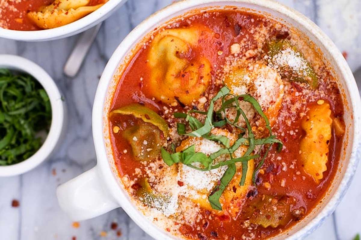 A bowl of tomato soup with tortellini in it.