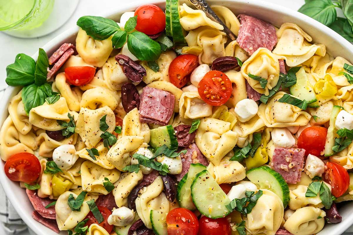 Tortellini salad with ham and tomatoes in a white bowl.