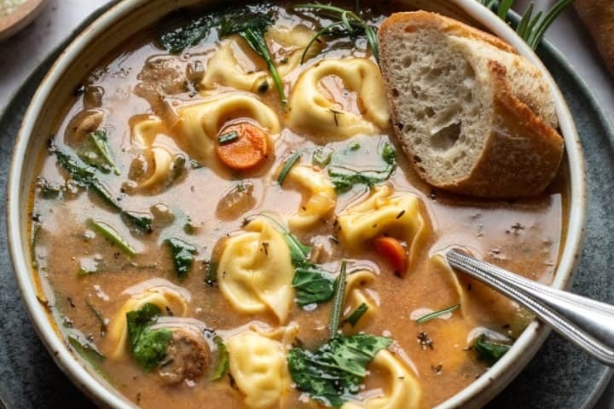 A bowl of tortellini soup with bread and spinach.