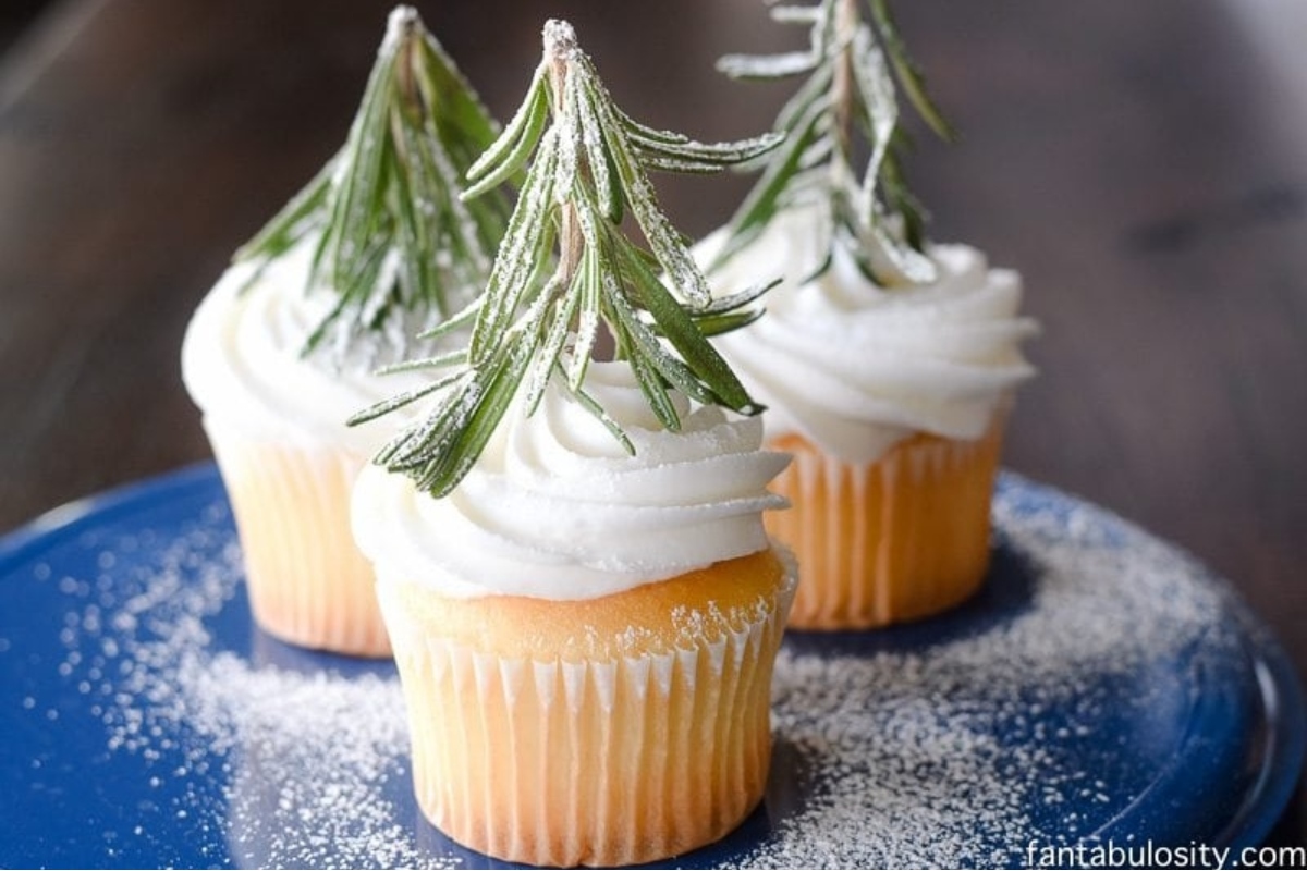Three Christmas cupcakes with sprigs of rosemary on top.
