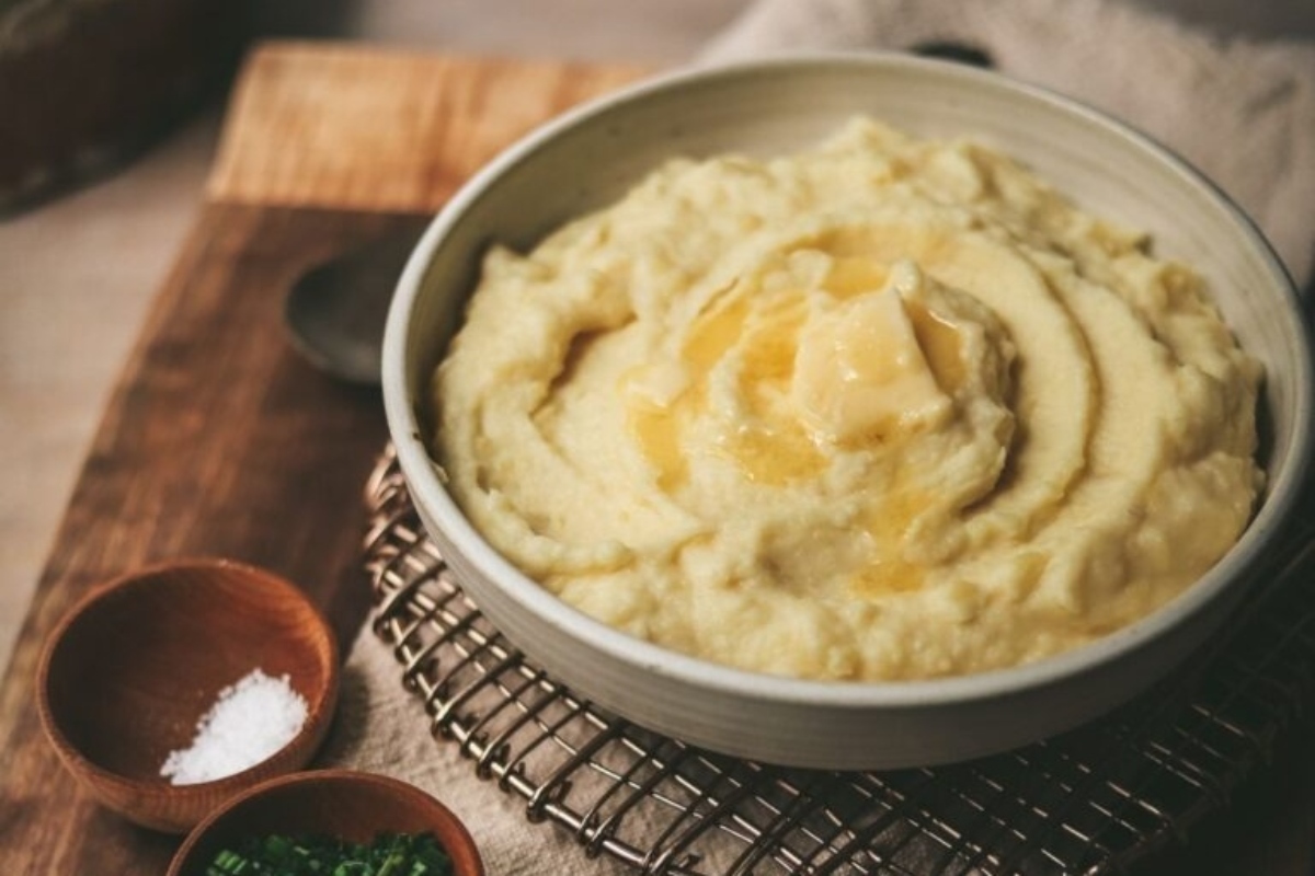 A bowl of mashed potatoes on a wooden cutting board.