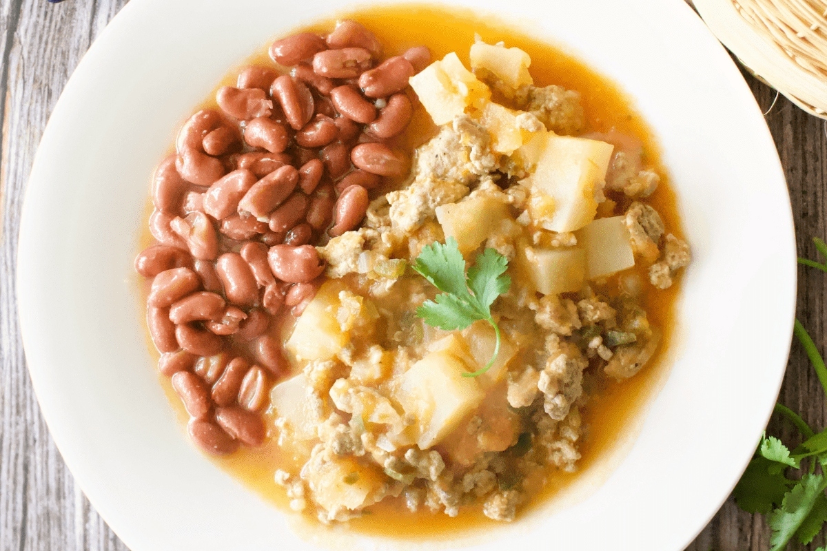A bowl of stew with beans, potatoes, and ground turkey on a wooden table.