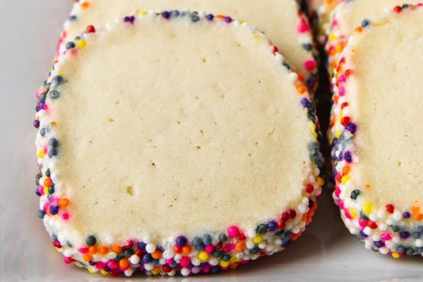 Three cookies with sprinkles on a white plate.