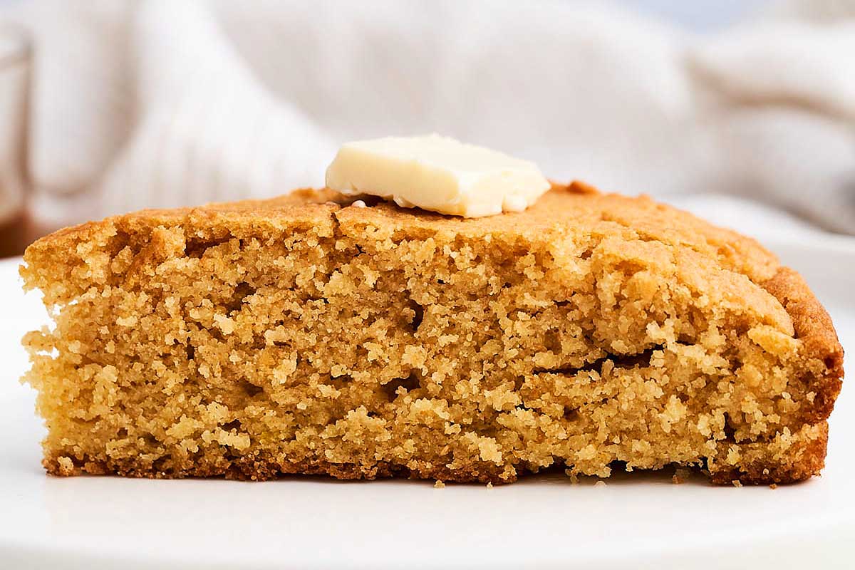 A slice of vegan cornbread with butter on a plate.