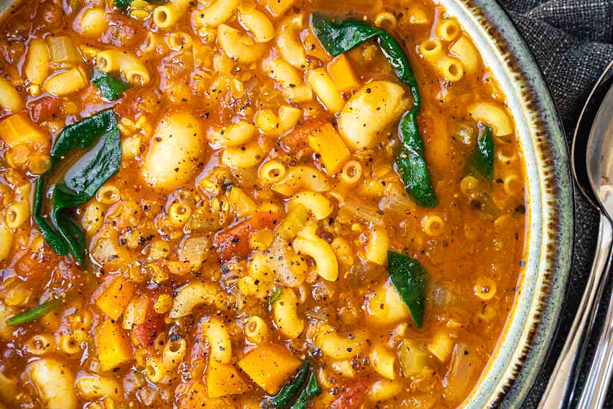 A bowl of pasta and vegetable soup with a spoon.