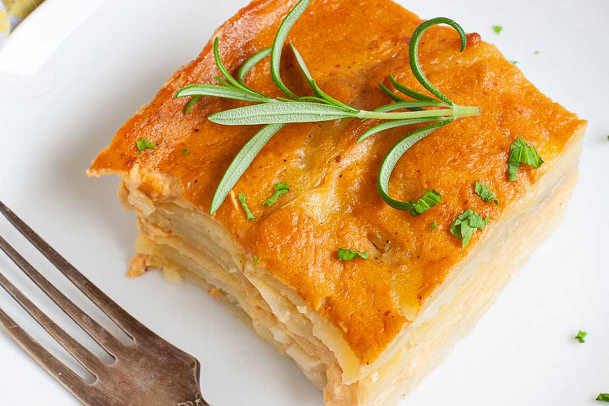 A vegan slice of potato casserole on a plate with a fork.