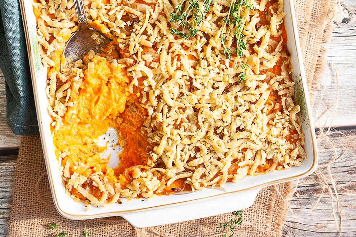 Vegan sweet potato casserole in a baking dish with a spoon, perfect for Thanksgiving.
