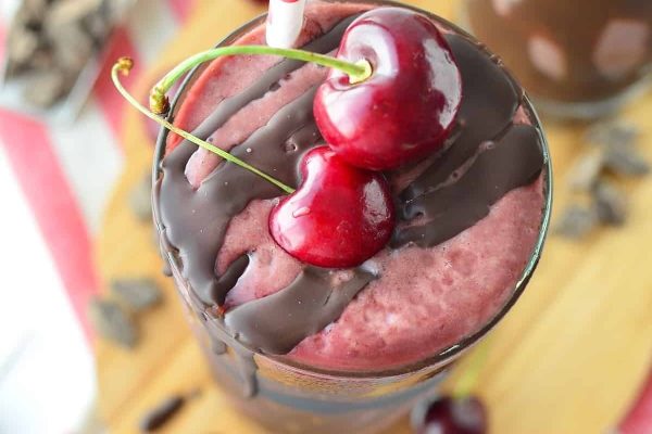 A milkshake with chocolate and cherries on a wooden cutting board.