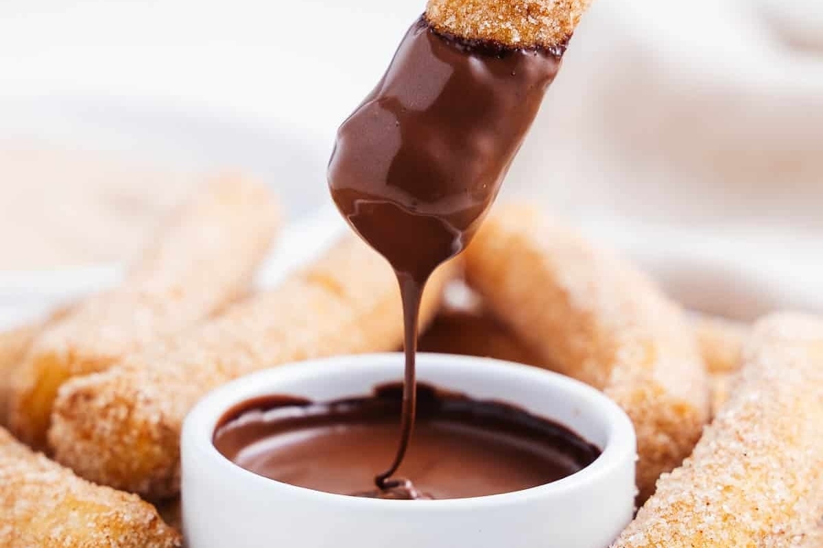 A cinnamon-infused chocolate dipping sauce being poured over fried doughnuts in this delectable recipe.