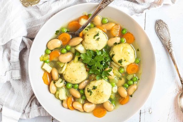 A bowl of soup with dumplings, peas and carrots.