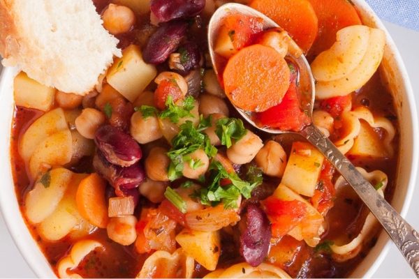 A bowl of bean and pasta soup with a spoon.