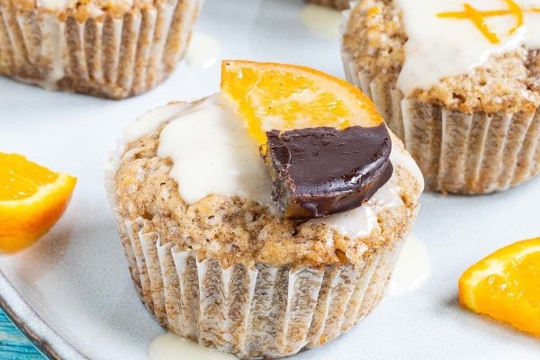 A plate of muffins with orange slices and icing. The muffins can be made using various recipes, and the addition of fresh orange slices on top adds a refreshing twist. The icing enhances
