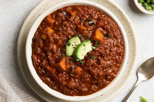 A bowl of chili with a spoon next to it.