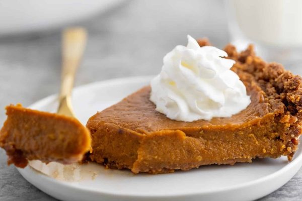 A slice of pumpkin pie with whipped cream on a plate.