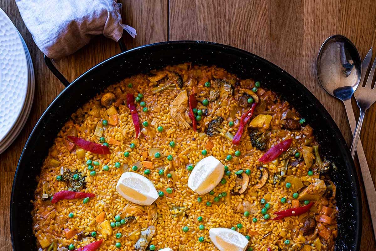 A pan full of paella on a wooden table.