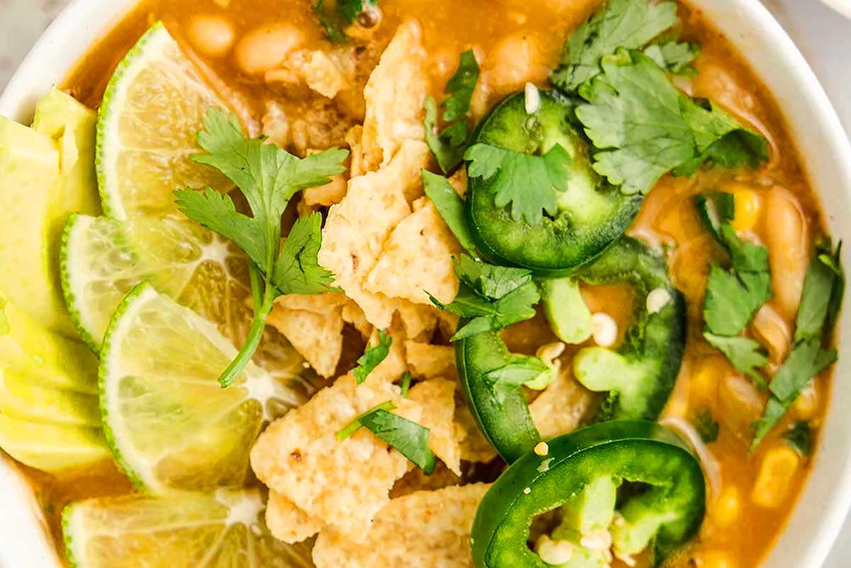 A bowl of mexican soup with tortilla chips and lime wedges.