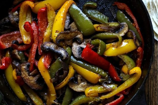 Peppers and mushrooms in a skillet on a table.