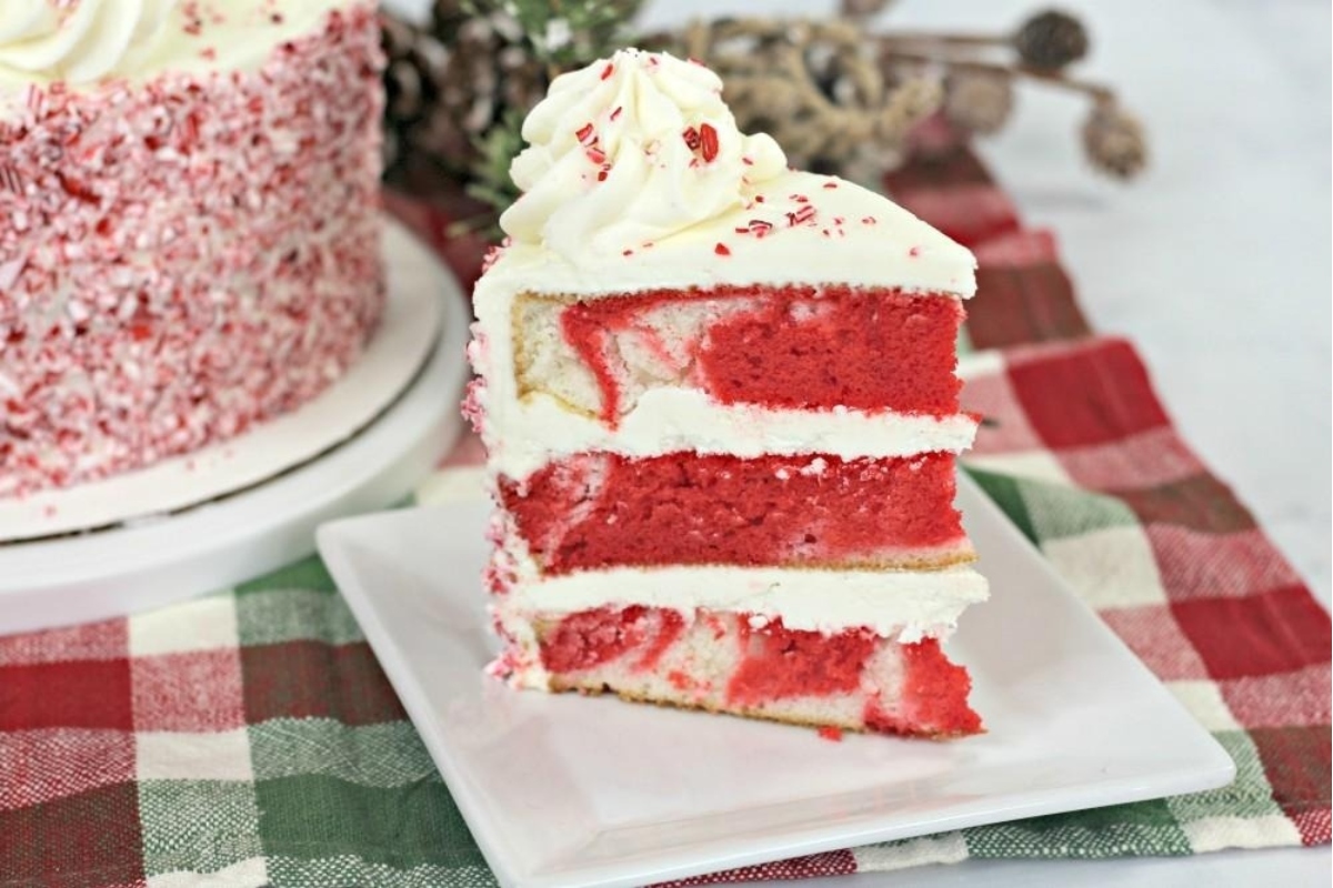 A slice of red velvet cake topped with a candy cane decoration on a plate.