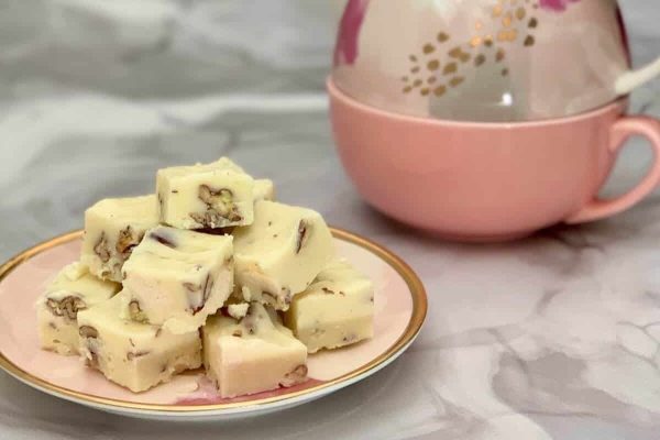 A plate of white fudge sitting next to a cup of tea.
