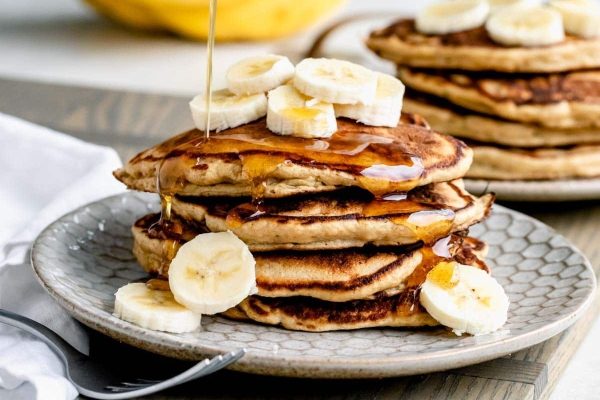 A stack of pancakes with syrup and bananas on a plate.