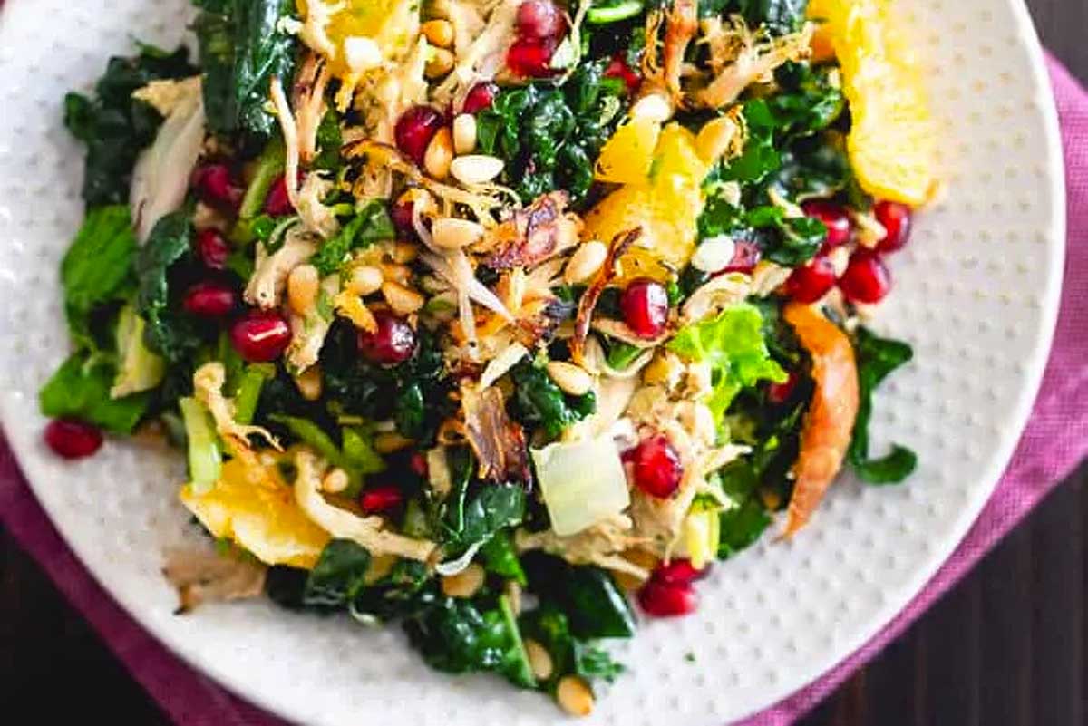 A plate of kale salad with chicken and pomegranate.