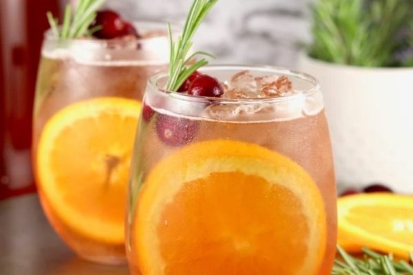 Two glasses of cranberry mulled wine with orange slices and rosemary sprigs.