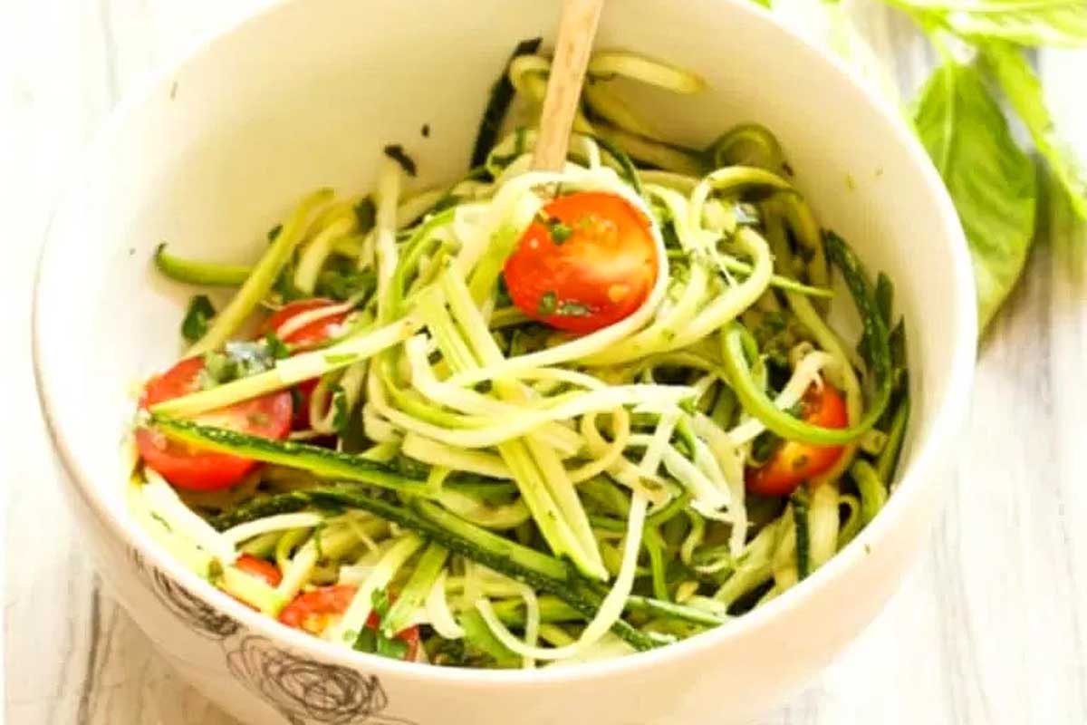 Zucchini noodles topped with fresh tomatoes and basil in a bowl.