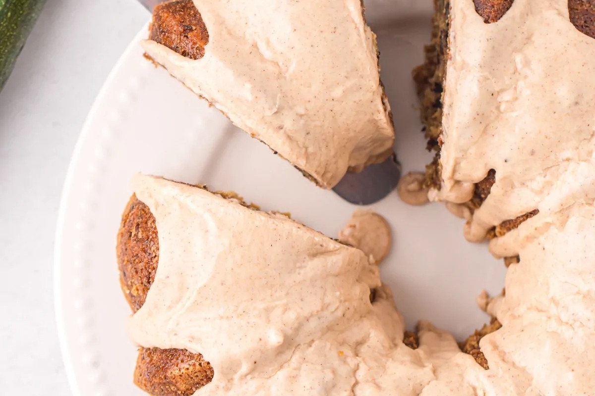 A mouthwatering zucchini bundt cake, sprinkled with cinnamon, displayed on a plate with a tantalizing slice taken out.